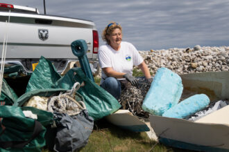 Michele Klimczak, the coastal debris coordinator for the Fishers Island Conservancy, sits in front of a day’s haul of garbage, nearly 150 lbs, collected over a few hours on a Fishers Island, New York beach. She weighs and records the trash she collects, the record of which is available to view on https://www.ficonservancy.org/