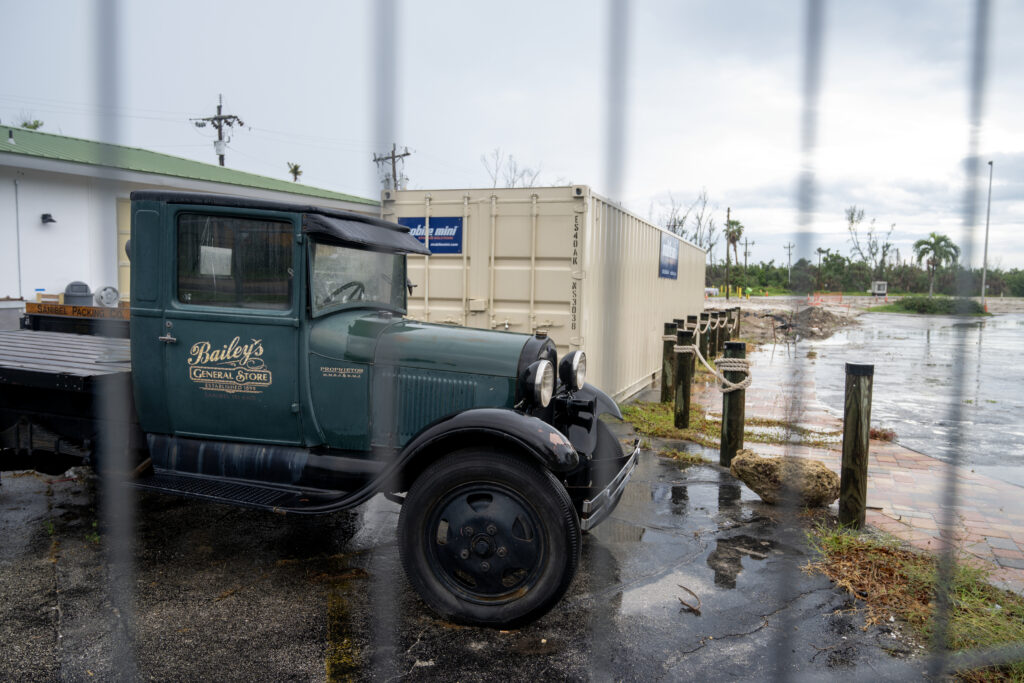 Behind a fence is the vacant lot that stands before all that remains of Bailey’s General Store after the strong winds and historic floods of Hurricane Ian. The historic location is now occupied by two antique trucks belonging to the store. Credit: Chris Tilley