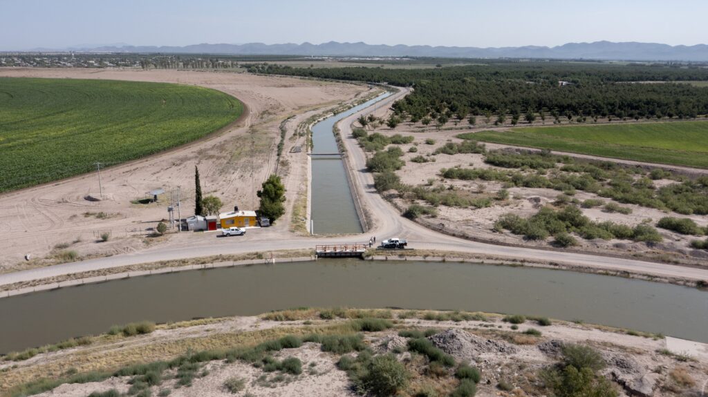 The principal irrigation canal of the Delicias district, in the foreground, connects with a smaller canal. Conchos River water feeds alfalfa and pecan production in August 2023.