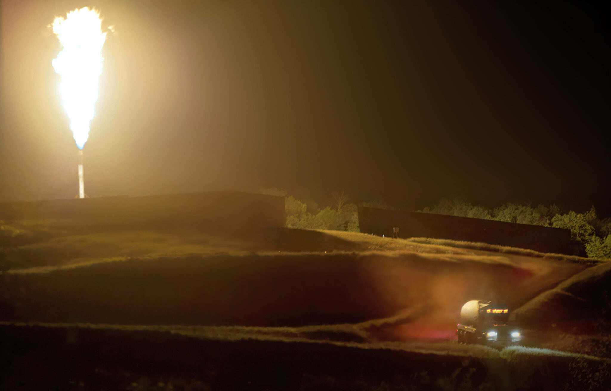 A truck filled with gas departs a newly completed gas well. The flare is burning because the infrastructure to transport the gas via pipelines was not yet complete. Credit: Scott Goldsmith